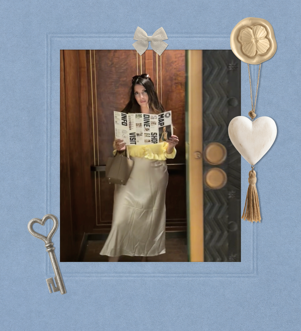 A woman stands in a doorway holding a magazine, wearing a long satin-like beige skirt and a yellow ruffled top. The photo is presented within a decorative blue frame with a key, bow, wax seal, and heart ornament.